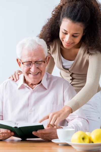 Caregiver smiling over the shoulder of smiling senior man | Neighborly Home Care