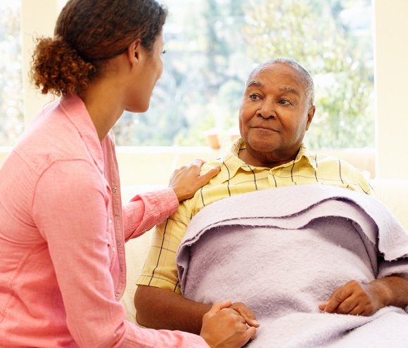 Caregiver sitting with elderly man who is holding a cane | Respite care services give time for family caregivers to recharge their energy and handle other pressing needs. | Neighborly Home Care