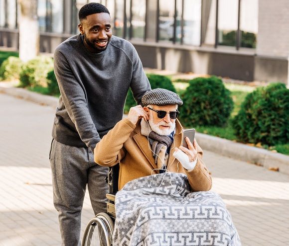 Caregiver helping elderly man out of bed to a wheelchair| Home Health Care Agency | Neighborly Home Care