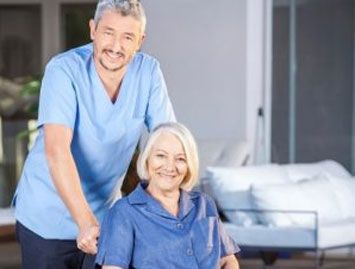 caregiver standing behind senior in a wheelchair | benefits of 24 hour senior home care | Neighborly Home Care