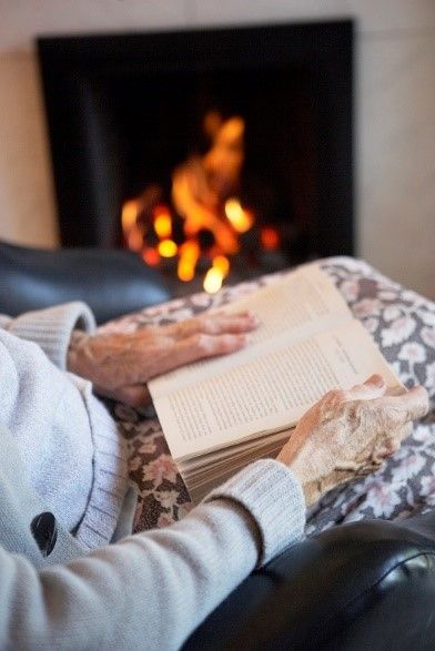 Senior sitting near fireplace reading book | senior care services | Neighborly Home Care