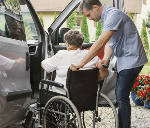 Caregiver helping elderly woman from wheelchair into a vehicle | Home Health Care Agency | Neighborly Home Care