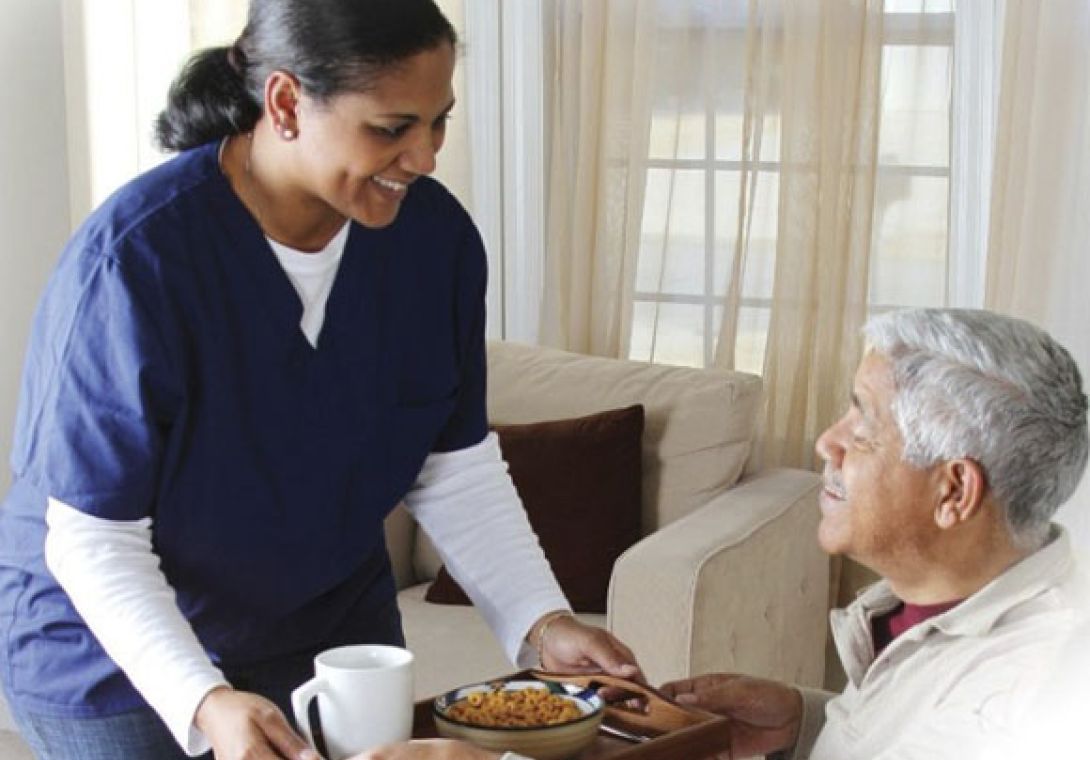 Caregiver in blue scrubs serving meal on a tray to elderly man | Philadelphia Home Care Agency | Neighborly Home Care