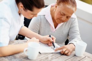 Caregiver providing respite care to senior woman doing crossword | Cost of Care at Neighborly Home Care