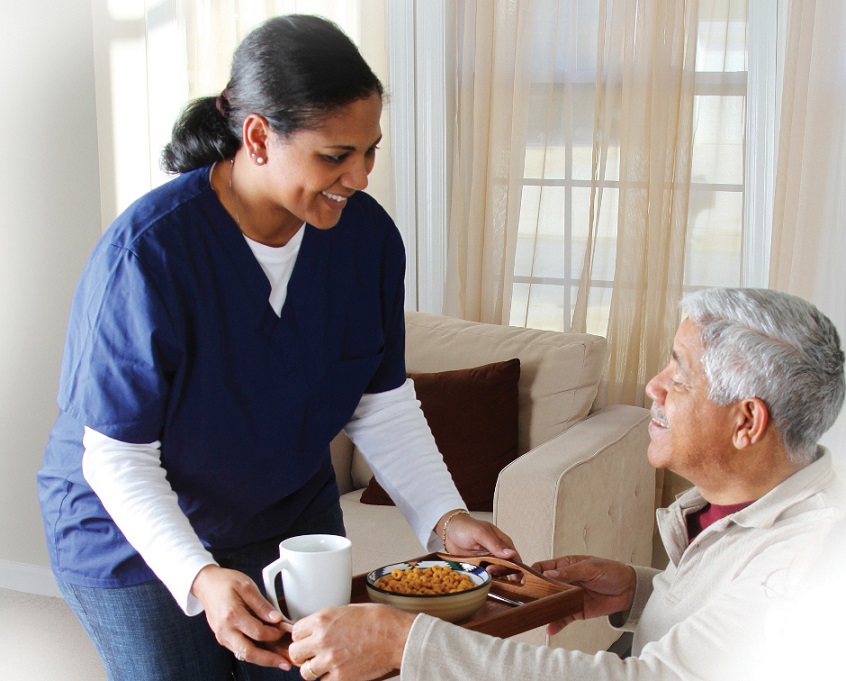 Female caregiver serving breakfast to senior man -Areas Served at Neighborly Home Care