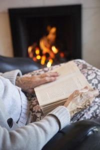 senior-woman-reading-book by the fire - elderly care winter tips - Neighborly Home Care