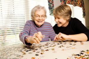 Woman working on puzzle with senior woman | The toll of caregiving on caregivers | Neighborly Home Care