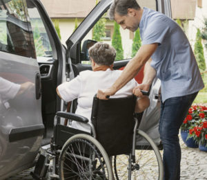 Caregiver helping elderly woman in wheel chair into care | care plans for seniors | Neighborly Home Care