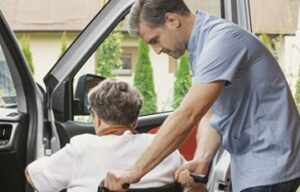 caregiver assisting senior woman from wheelchair into car | senior transportation services help alleviate one of the challenges seniors face living at home alone | Neighborly Home Care